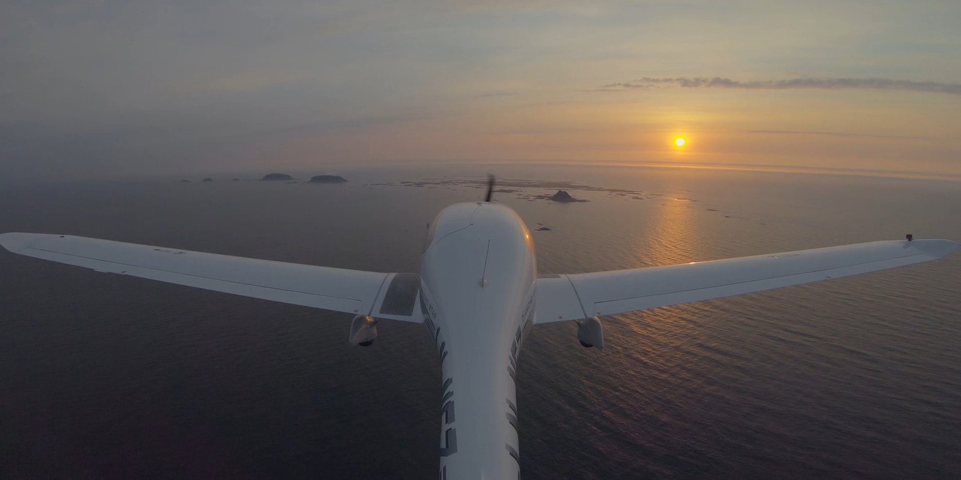 Light aircraft flying over the sea and into the horizon at sunset.